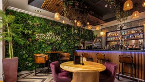Zona de bar con pared verde, mostrador de bar de madera y diversas opciones de asiento, incluyendo mesas redondas y taburetes.
