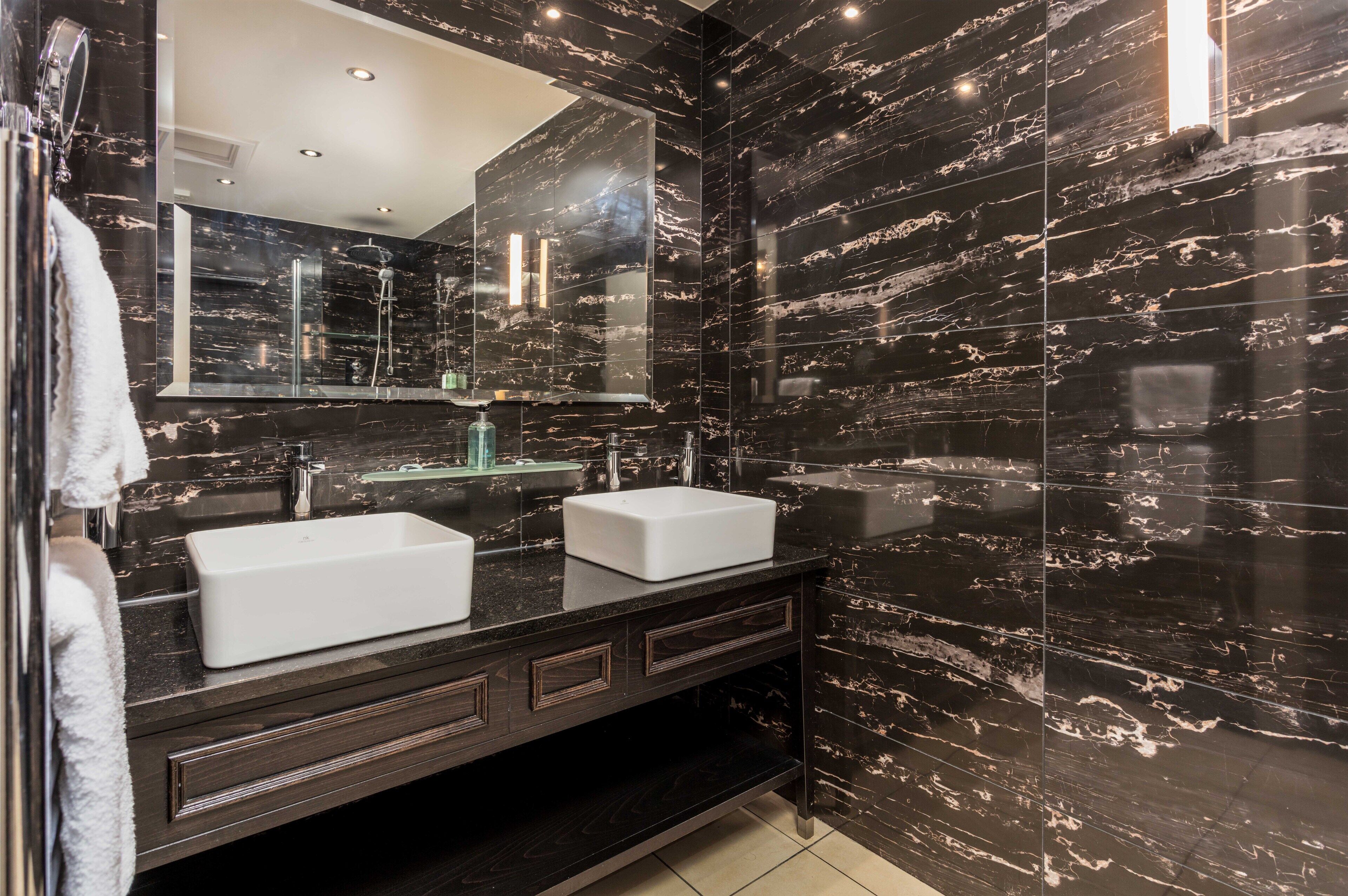 A modern bathroom with two sinks, dark marble walls, and a large mirror.