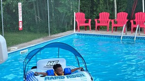 A pool with a water slide, red chairs, and a safety sign.