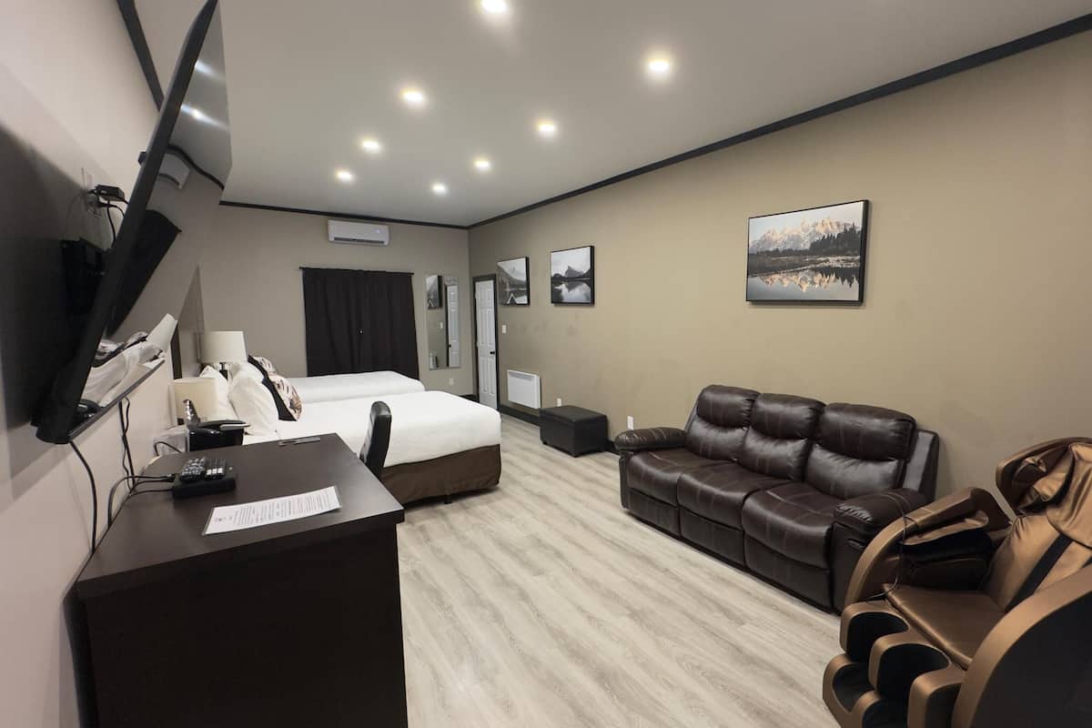 Habitación de hotel con cama, sofá de cuero, sillón de masajes, escritorio con computadora y televisor montado en la pared.