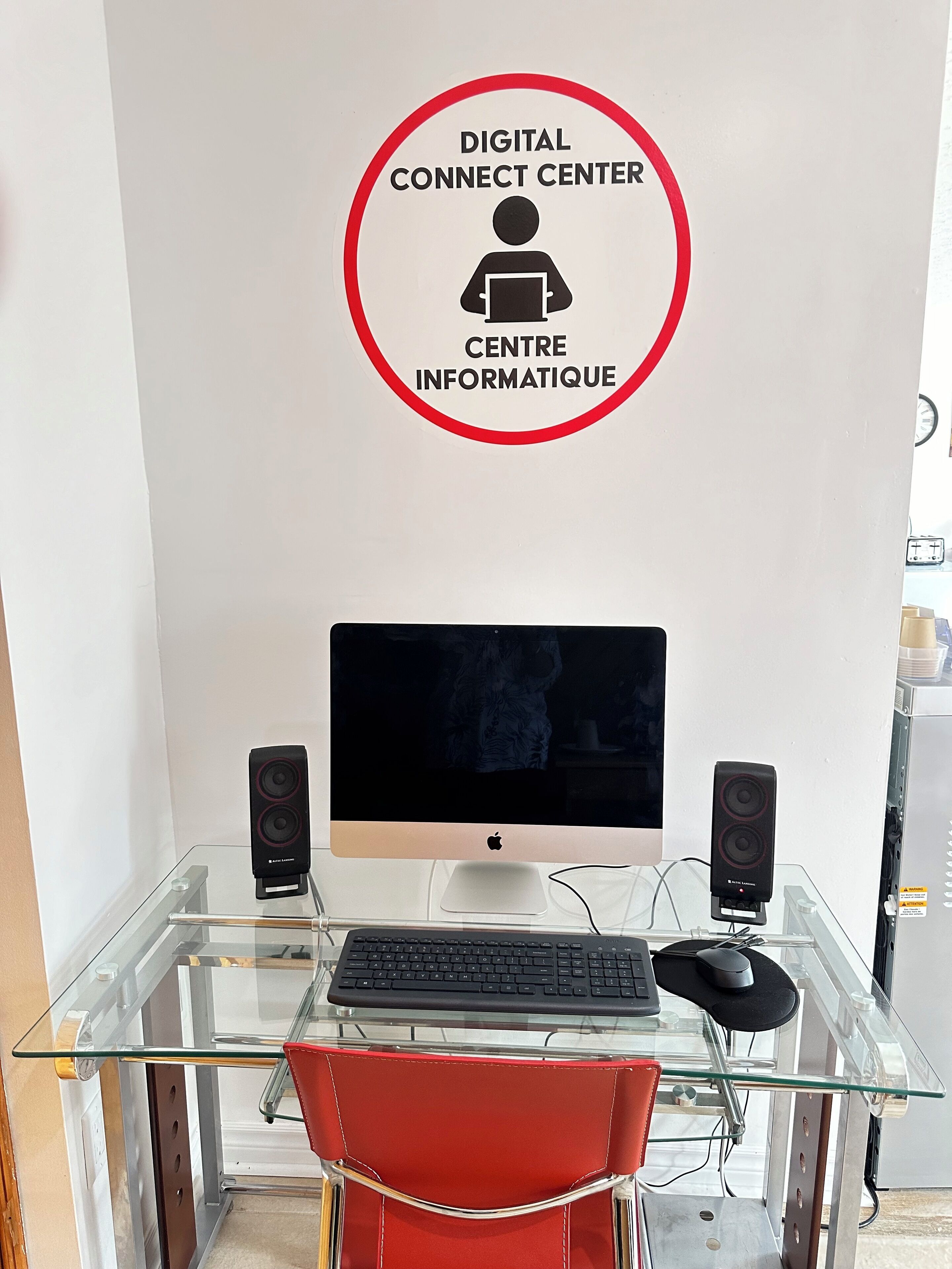 A workspace with a glass desk, a red chair, a computer monitor, two speakers, and a keyboard.