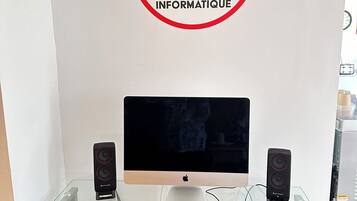 A workspace with a glass desk, a red chair, a computer monitor, two speakers, and a keyboard.