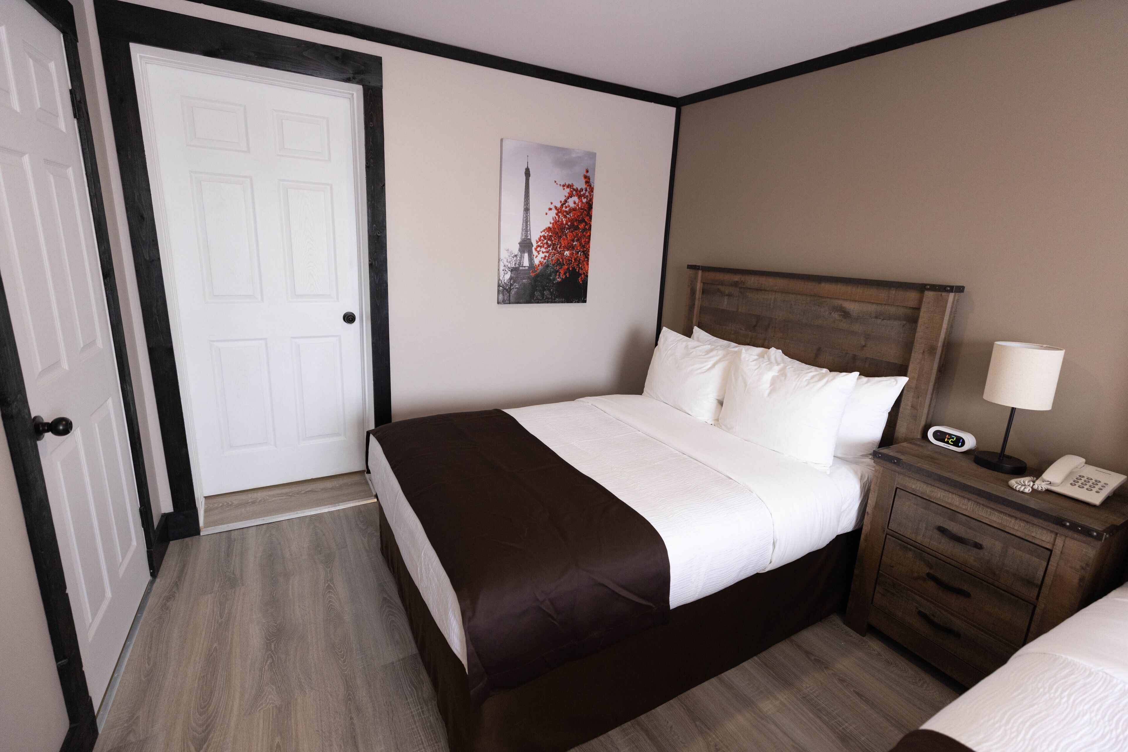 Habitación de hotel con cama, mesita de noche con teléfono, puerta y un cuadro colgado en la pared.