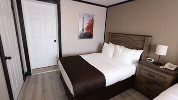 Habitación de hotel con cama, mesita de noche con teléfono, puerta y un cuadro colgado en la pared.