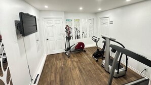 A gym with exercise equipment, white walls, and wooden flooring.