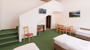 Una camera d'albergo con tappeto verde, una scala, un letto, una scrivania con sedie e due quadri alle pareti.