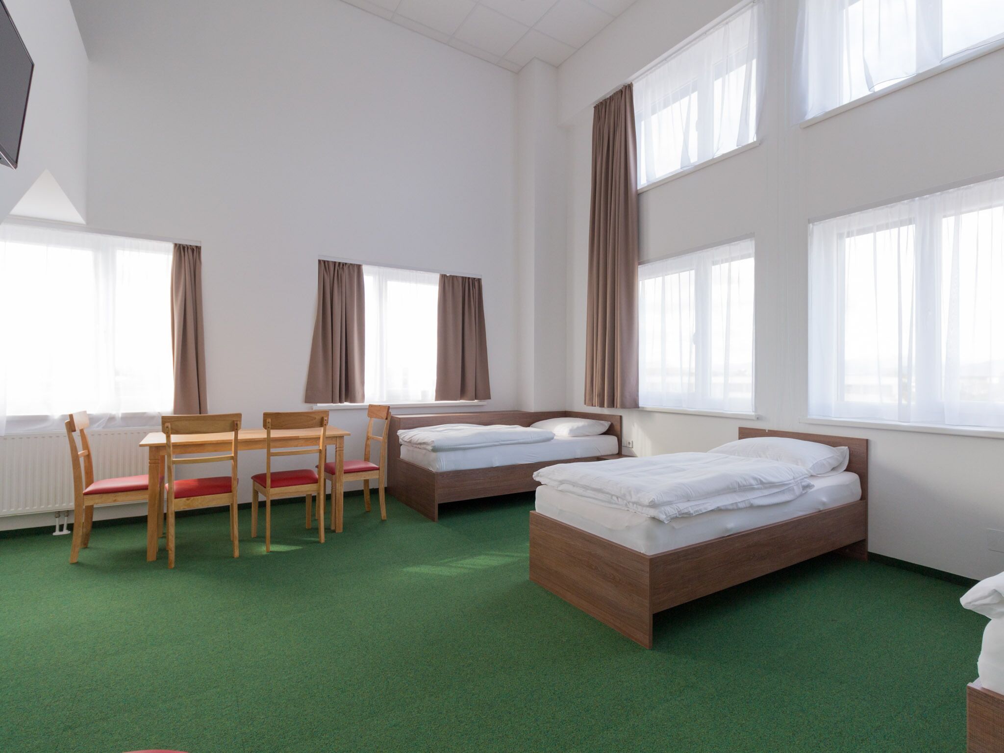 Habitación de hotel con dos camas, un escritorio, sillas y ventanas amplias.