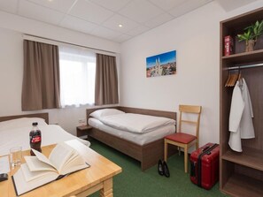 A hotel room with a bed, a desk with a book, a chair, a suitcase, and a coat rack. - Win Budget B&B (Wiener Neustadt)
