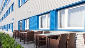 Esterno di un albergo con posti a sedere all'aperto, persiane blu e un vialetto lastricato.