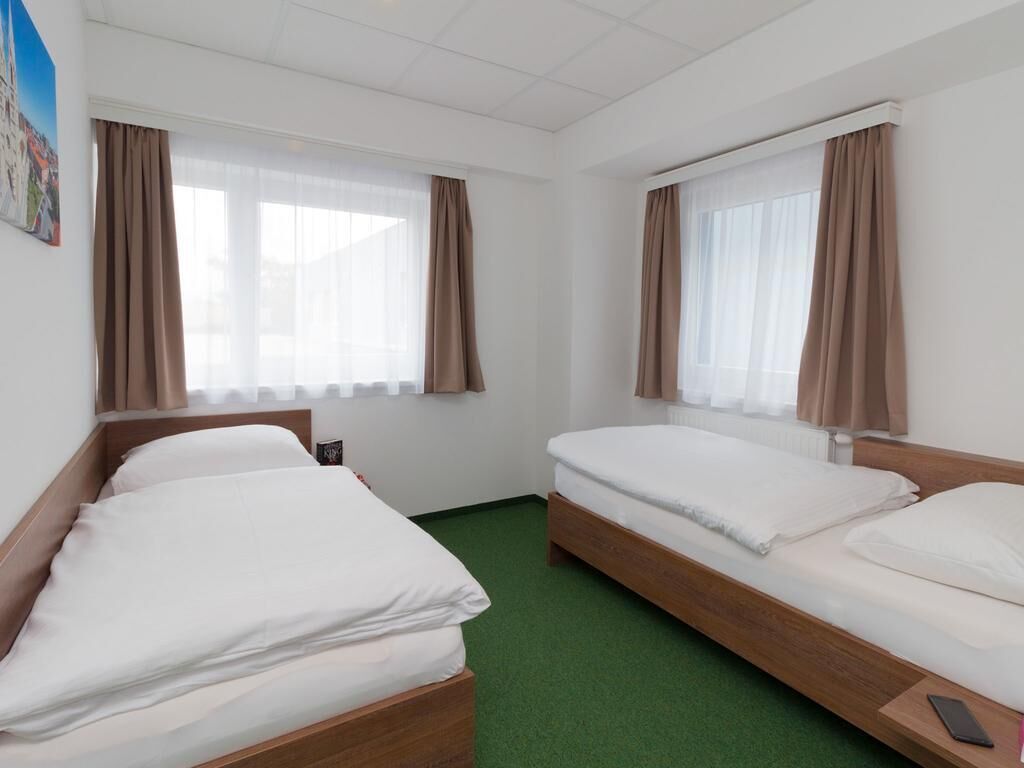 Une chambre d’hôtel avec deux lits simples, une moquette verte et un tableau au mur.