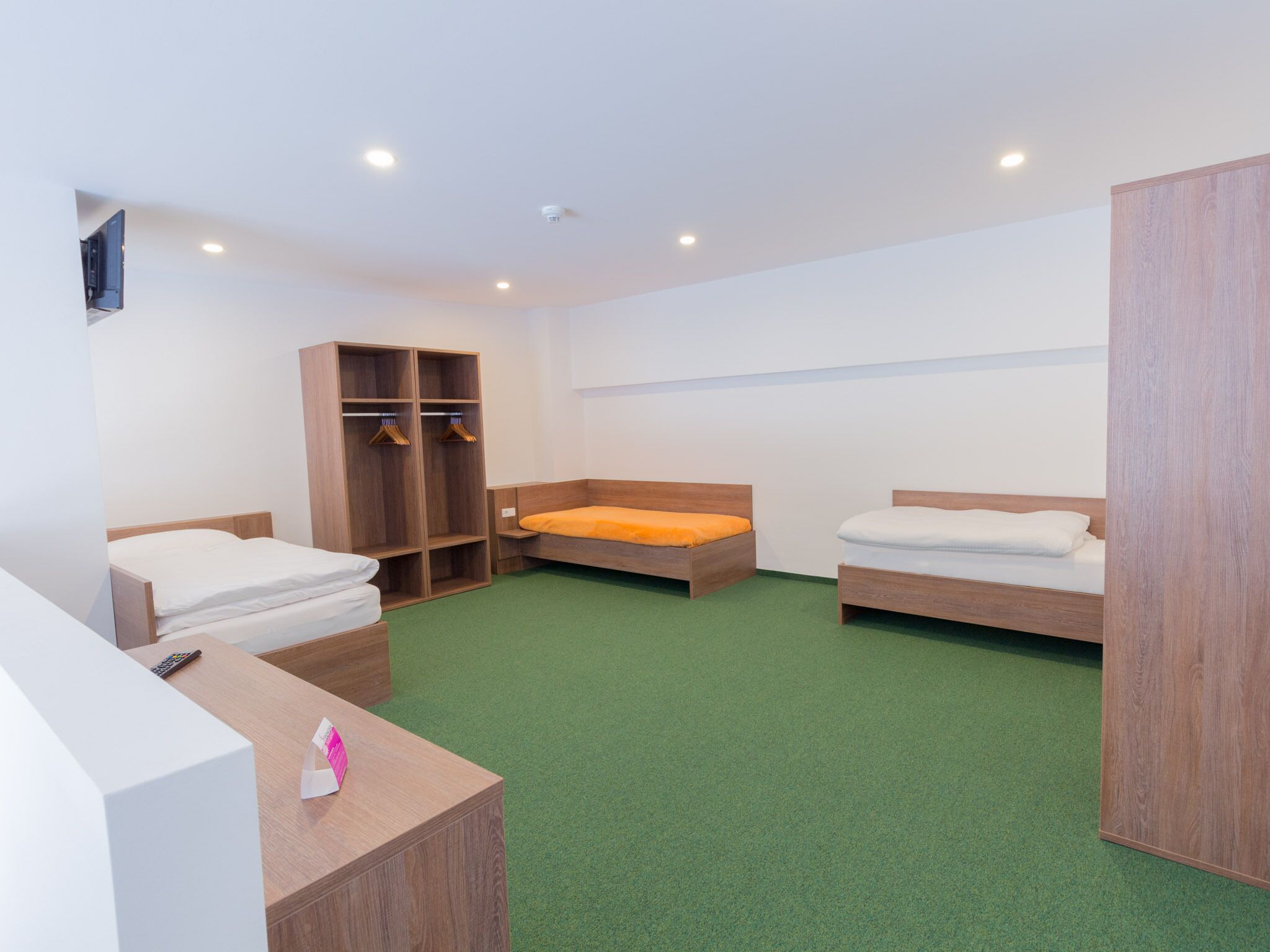 Quarto com duas camas de solteiro, guarda-roupa de madeira, escrivaninha com telefone e tapete verde.