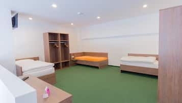 Quarto com duas camas de solteiro, guarda-roupa de madeira, escrivaninha com telefone e tapete verde.