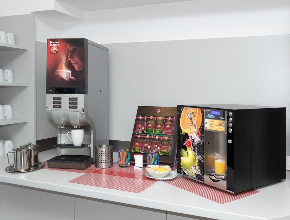 Una máquina de café con pantalla digital, un tablero de menú y varias tazas y recipientes para café sobre una encimera.