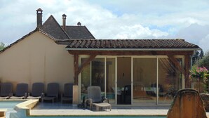 A pool area with lounge chairs and a covered seating area with a glass door. - Maison Périgourdine Avec vue Magnifique, sur les Hauteurs de Sarlat (SARLAT LA CANEDA)