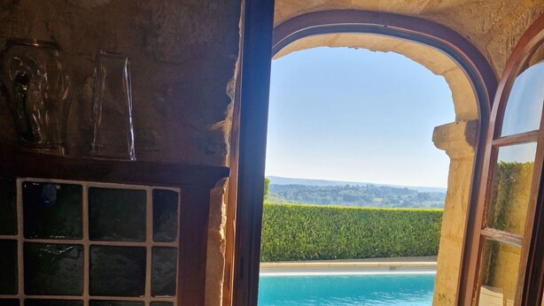 A rustic room with a stone wall, a window with an arched view overlooking a body of water and greenery. - Maison Périgourdine Avec vue Magnifique, sur les Hauteurs de Sarlat (SARLAT LA CANEDA)
