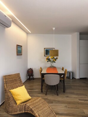 A modern living room with a wicker chair, a dining table with a vase of sunflowers, and a hanging light fixture.