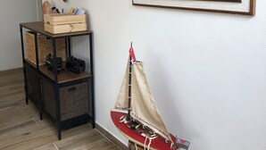 A room with a wooden floor, a small table with a model ship, a framed painting of the ocean, and a hanging decorative item. - Beautiful 2-bedroom apartment in Tirrenia (Tuscany) (Marina di Pisa-tirrenia-calambr)