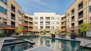 A modern apartment building with a central courtyard featuring a swimming pool, lounge chairs, and umbrellas. - Sexy & Sensual 1BR Escape (Dallas)