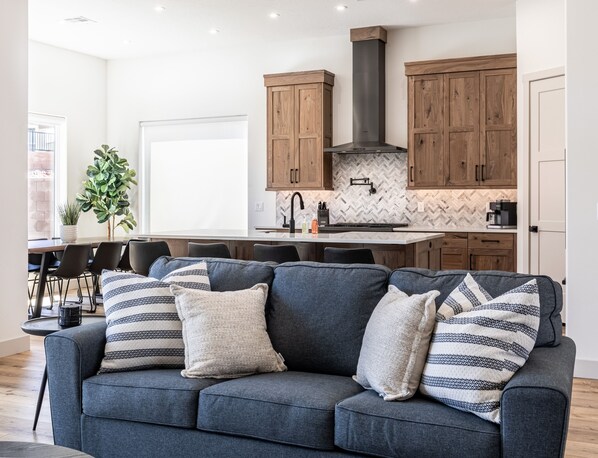 Una sala de estar moderna con un sofá gris, armarios de madera y una cocina con salpicadero de espiga.