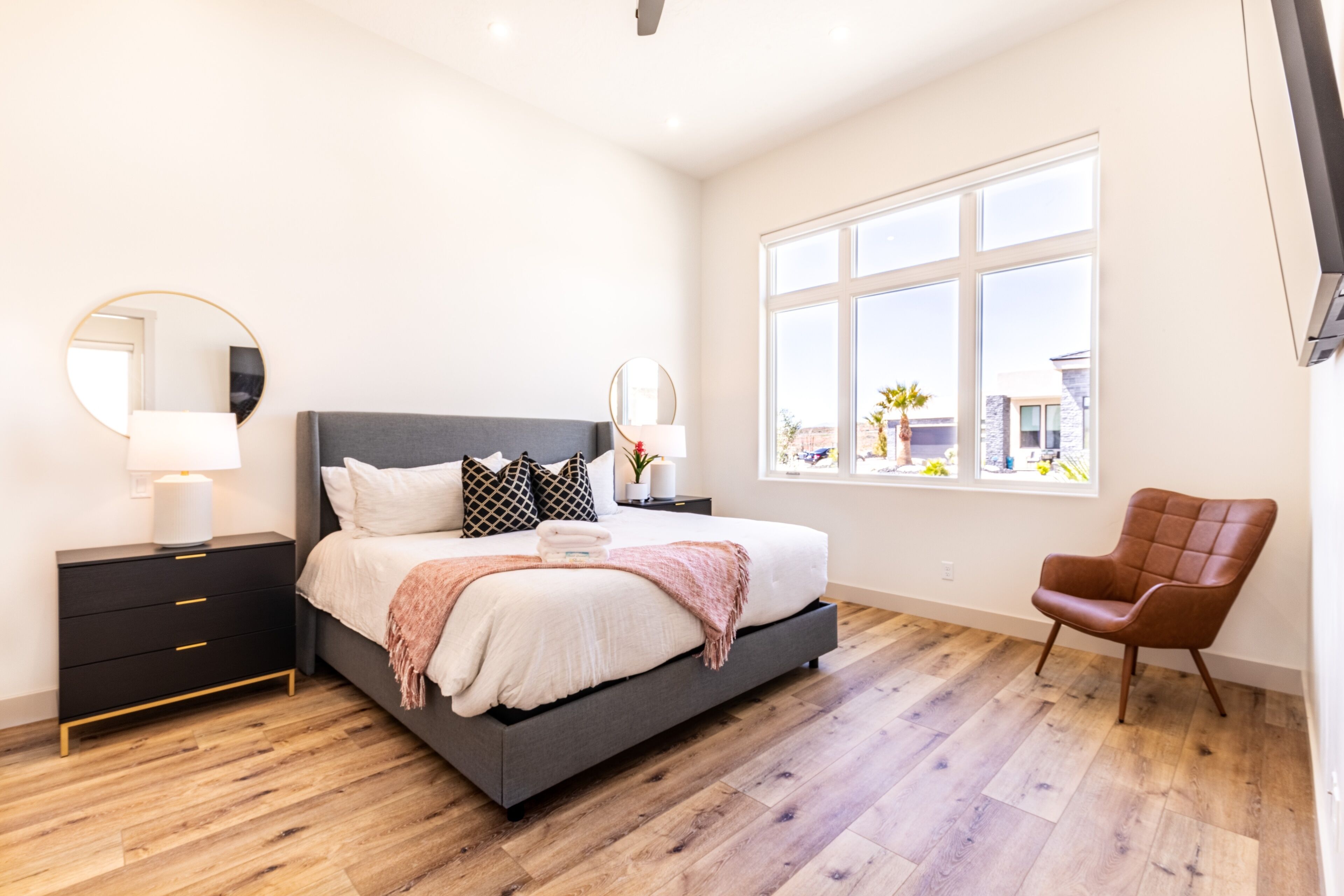 Une chambre moderne avec un grand lit, des tables de chevet, un fauteuil et une fenêtre donnant sur un beau paysage.