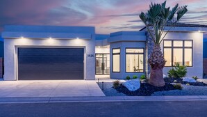 A modern two-story house with a garage, large windows, and a well-maintained garden with rocks and a palm tree.