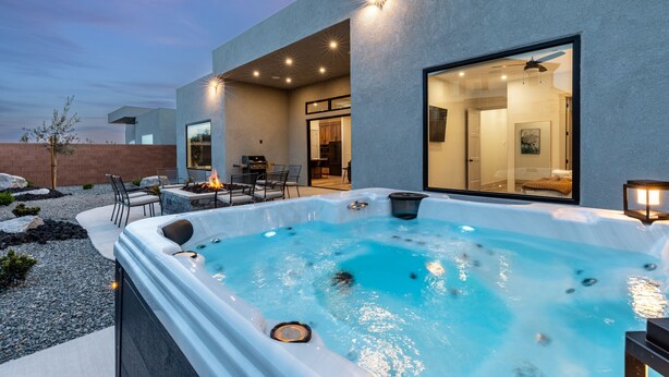 A modern outdoor hot tub area with a fire feature, seating, and a glass-enclosed room.