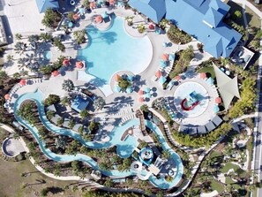 Vista aérea de un complejo turístico con una amplia piscina central, varias toboganes de agua y tumbonas.