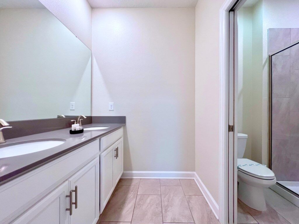 A modern bathroom with a dual sink vanity, a toilet, and a glass shower enclosure.