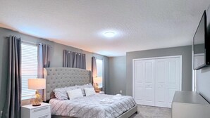 A bedroom with a tufted headboard bed, bedside tables, a wardrobe, and a flat-screen TV. - Spacious Home With Fun Decore And Game Room-4544tb 8 Bedroom Home by RedAwning (Kissimmee)