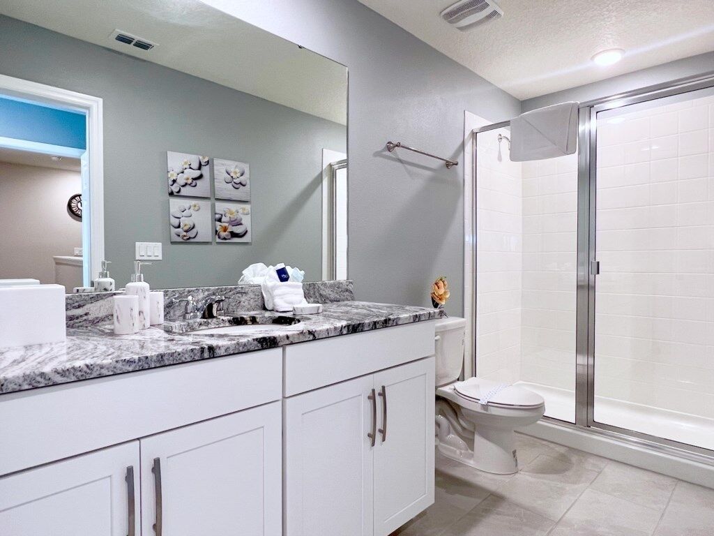 A modern bathroom with a marble countertop, white cabinets, a glass shower enclosure, and a toilet.