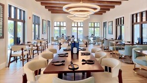 Un amplio comedor con mesas y sillas largas, ventanas grandes y techo de madera.