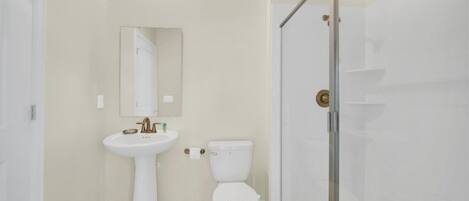 Baño con lavamanos blanco, inodoro y cabina de ducha de vidrio.