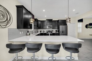 Una cocina moderna con armarios oscuros, una isla blanca y tres taburetes negros.