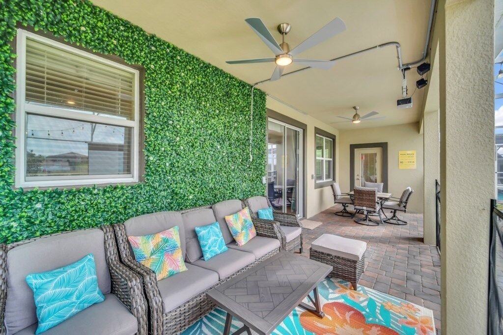 An outdoor patio area with a green wall, wicker furniture, and ceiling fans.