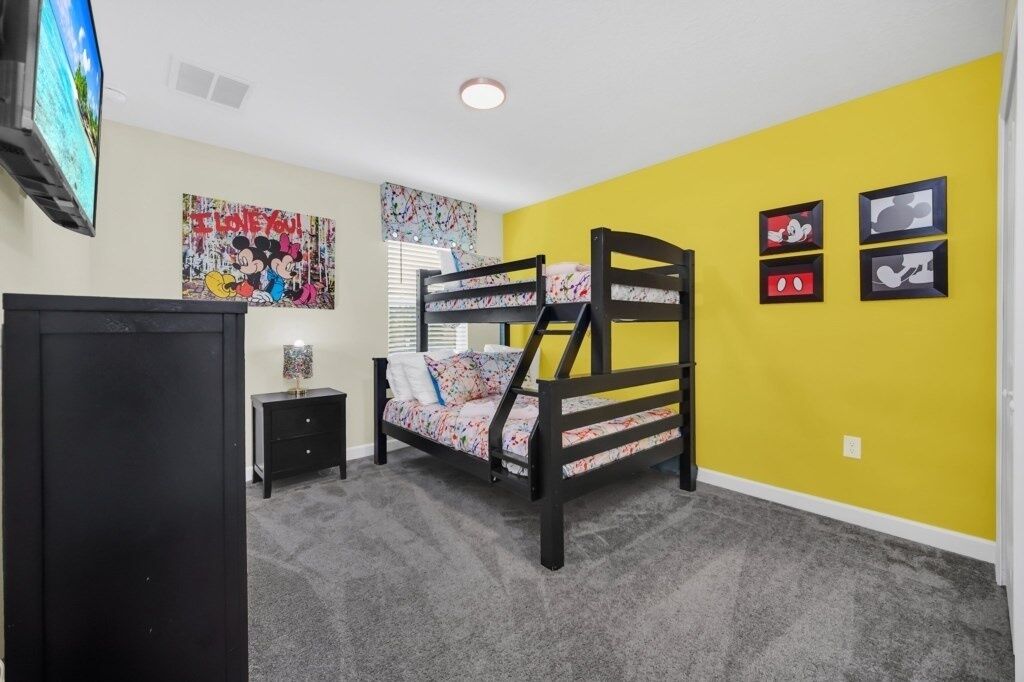 Un dormitorio con una litera, un escritorio pequeño, un televisor y decoración en la pared.