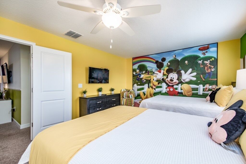 A bedroom with two beds, a ceiling fan, a large Disney-themed mural, and a white door.
