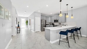 A modern kitchen with a central island, bar stools, and pendant lighting. - 9 Bed Home With Theme Bedrooms Game Room,Pool Spa 9 Villa by RedAwning (Davenport)