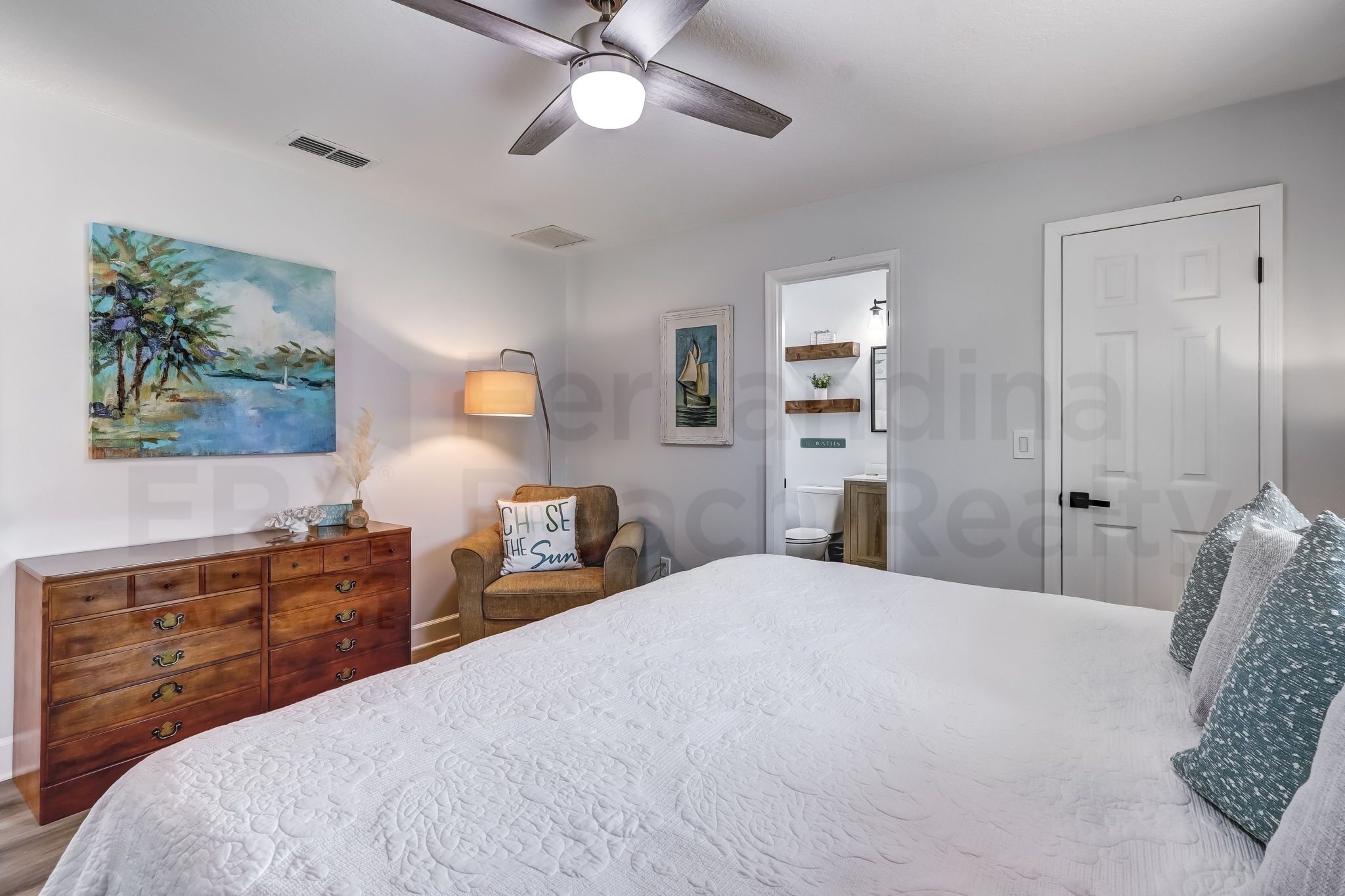 A bedroom with a bed, a ceiling fan, a dresser, a chair, and a painting on the wall.