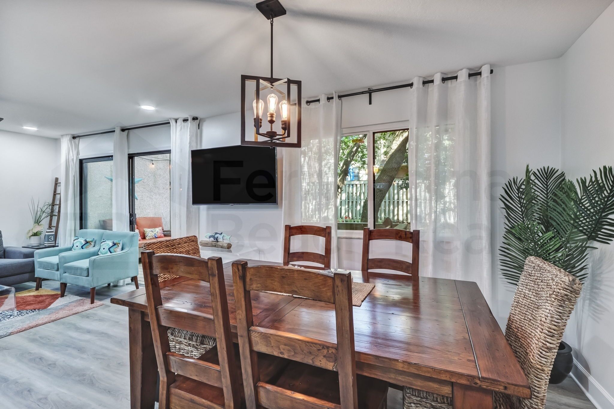A dining area with a wooden table and chairs, a hanging light fixture, and a large window with curtains.