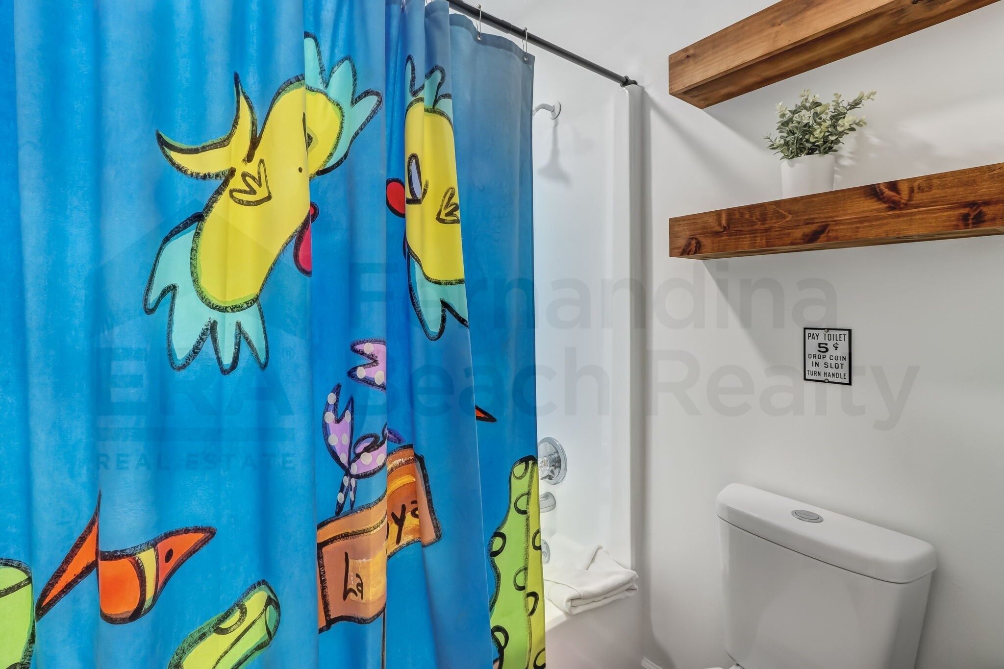 Une salle de bain avec un rideau de douche orné de personnages de dessins animés, des toilettes et une petite plante posée sur une étagère.