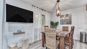 A dining area with a wooden table and wicker chairs, a mounted TV, and a potted plant.