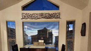 A dining area with a table and four chairs, a large window with blinds, and a ceiling fan. - Odysea Modern Ocean Cabin 26 w/ Jacuzzi & Modern Decor (Private Beach Owned by White Rock Resort) (Smith River)