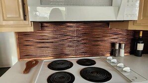 A kitchen with a white stove, a microwave, and copper backsplash. - Odysea Modern Ocean Cabin 26 w/ Jacuzzi & Modern Decor (Private Beach Owned by White Rock Resort) (Smith River)