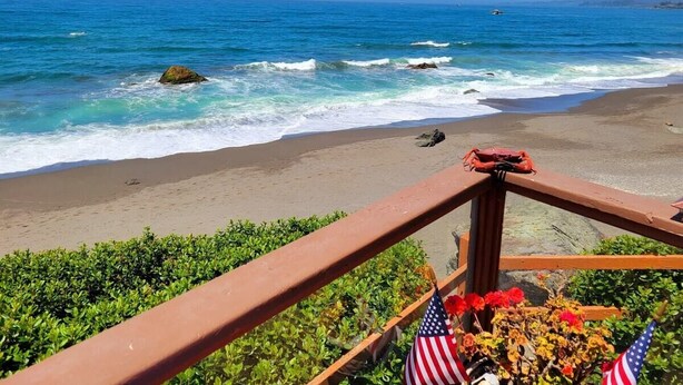 Een uitzicht op het strand met een houten hekwerk, Amerikaanse vlaggen en een helderblauwe lucht.