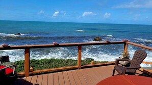 Een houten terras met uitzicht op de oceaan, met een leuning en twee stoelen.