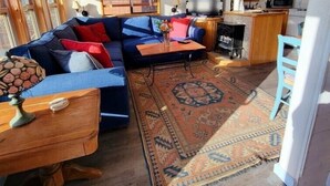Een gezellige zithoek met een blauwe bank, houten kasten, een keuken met een magnetron, en een plafondventilator.