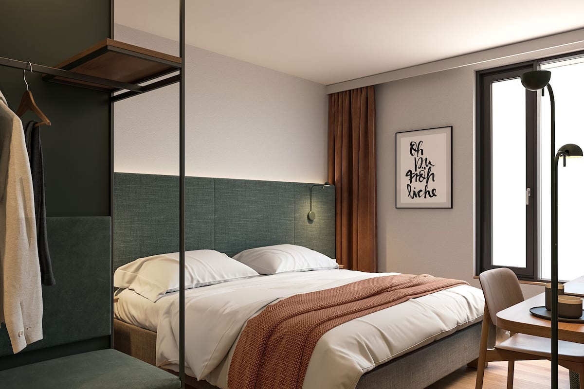 Ein modernes Hotelzimmer mit einem Bett, einem Schreibtisch, einem Stuhl, einem Kleiderschrank und einem Vorhangfenster.