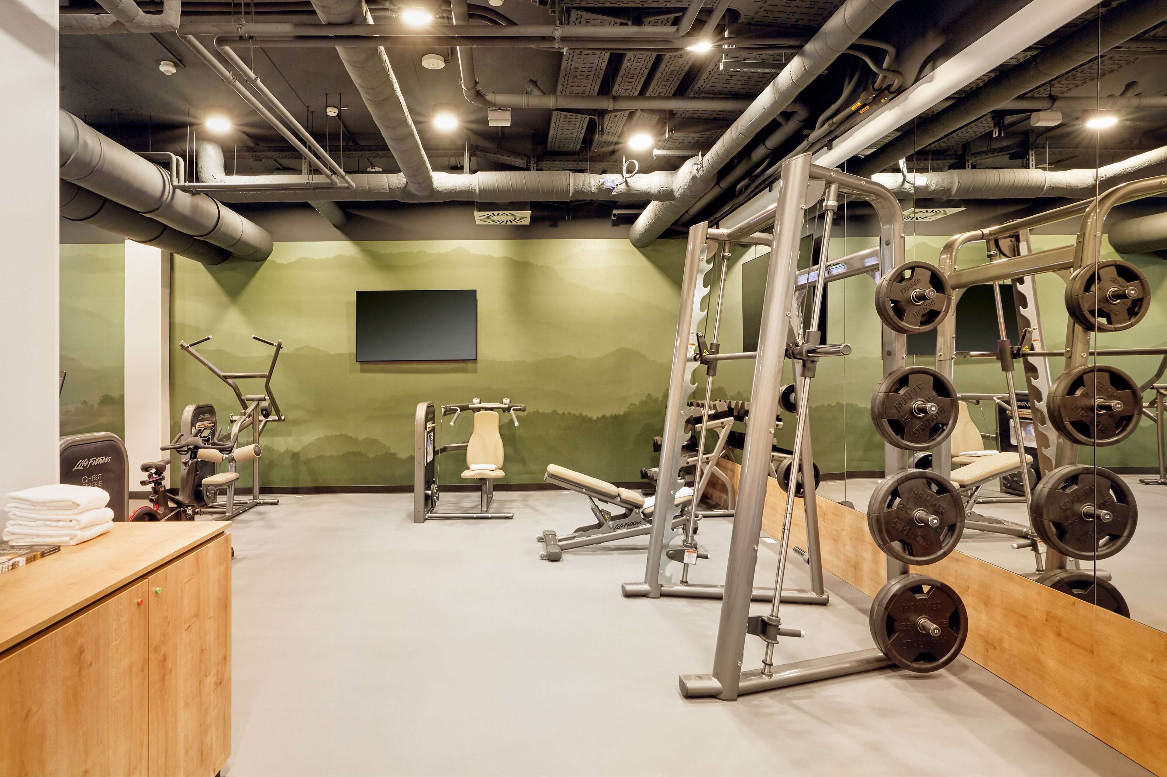 A gym with weightlifting equipment, a bench press, and a wall-mounted TV.