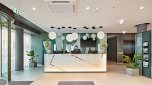 Un área de recepción de hotel moderna con un escritorio de vidrio, una recepcionista y una pantalla digital.