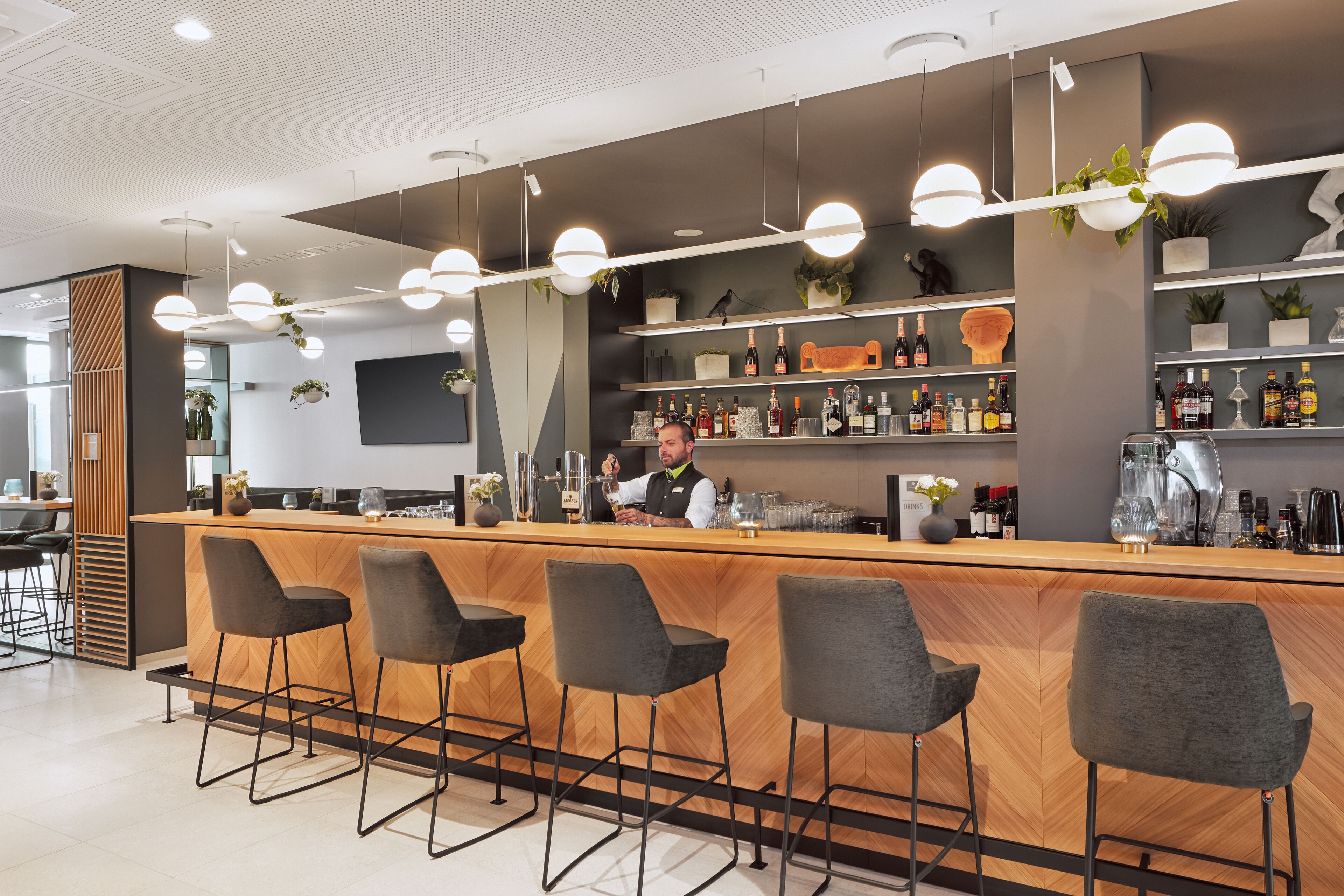 Zona bar moderna con un bancone in legno, sgabelli da bar e scaffali pieni di bottiglie.